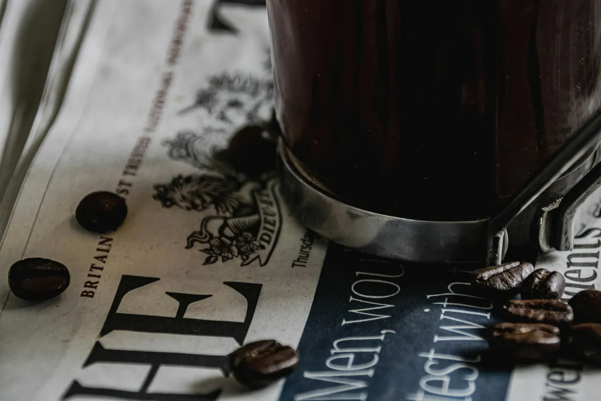A cup of coffee and scattered coffee beans resting on a folded newspaper, representing open, flexible investing.