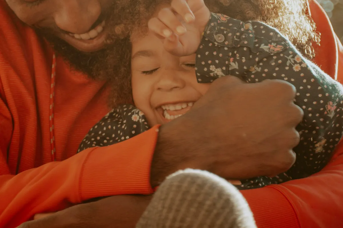 A father warmly embracing his laughing child in golden sunlight, representing dignified, supportive family care.