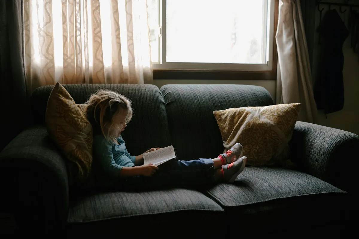 A child reading a book by a sunlit window, representing education savings for the future.