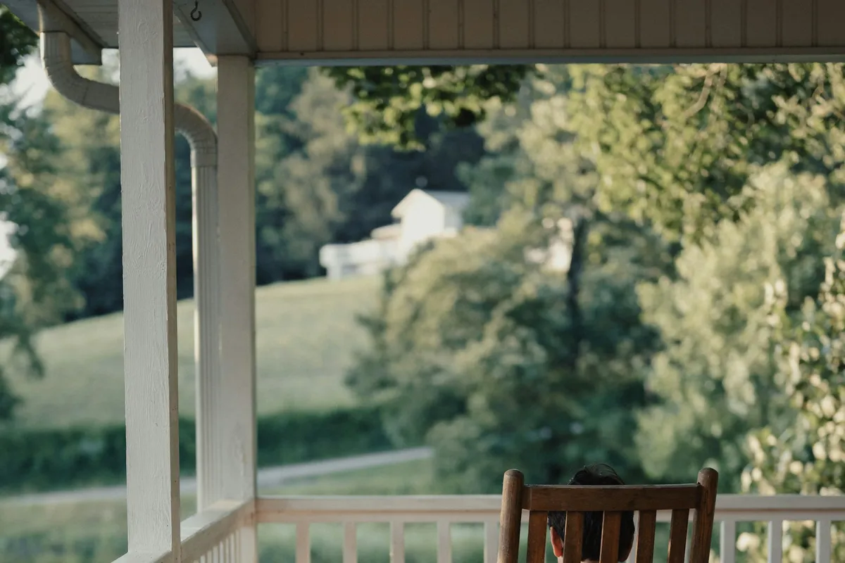 A person relaxing in a rocking chair on a porch overlooking green fields at golden hour, representing calm retirement income.