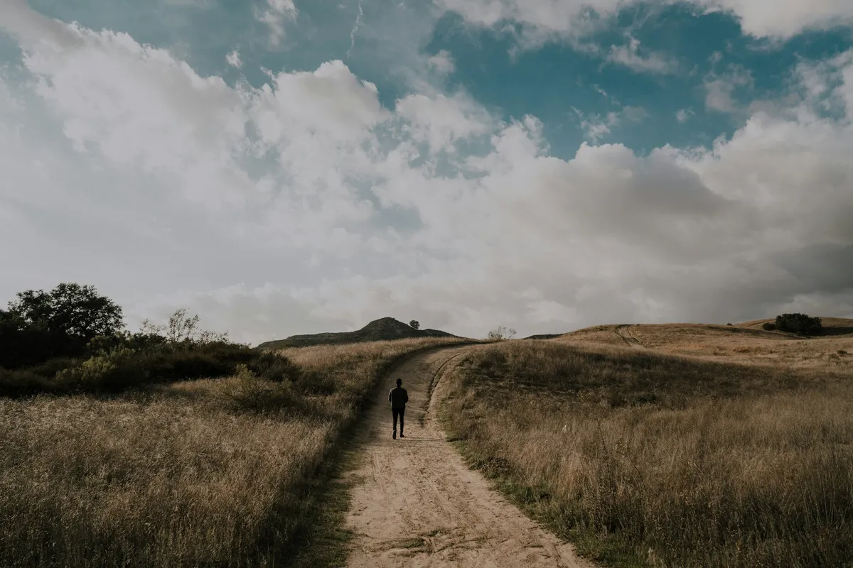 A person walking along a long dirt path toward distant hills, representing a steady, long-term retirement horizon.